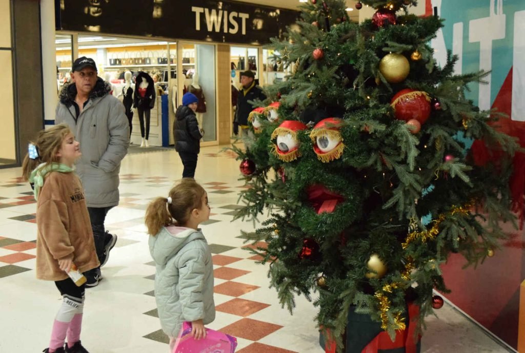 A performer dressed as a christmas tree interacts with two children