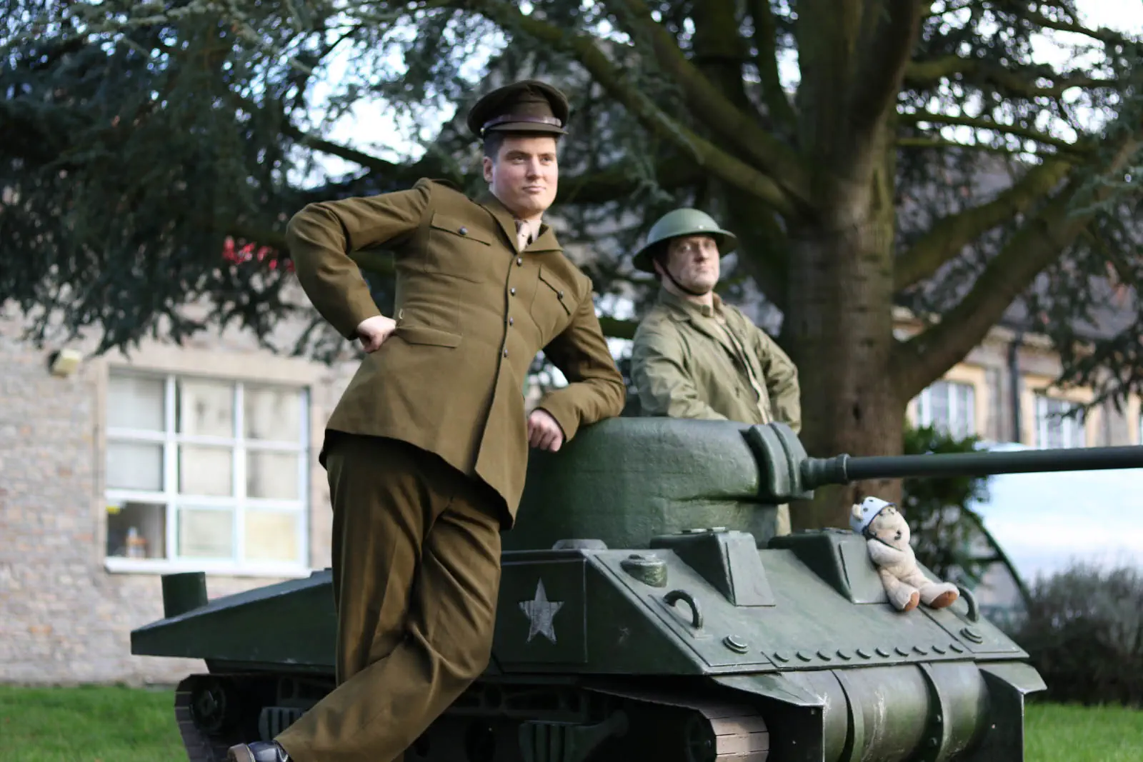 Military walkabout act featuring a realistic mini tank. Two performers in military garb lean casually on the tank.