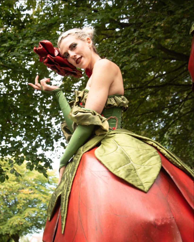 A striking rose stilt walker dressed in a green leafy corset with a large rose shaped skirt.